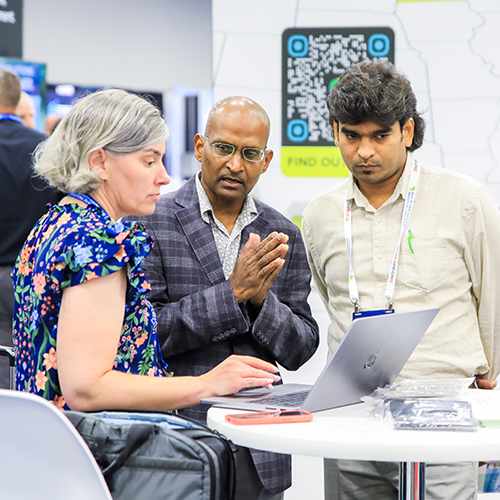 three people standing and talking while looking at laptop on table