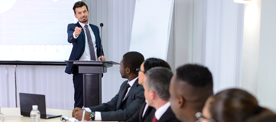 man at podium speaking to others at table